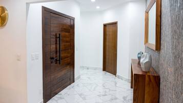 A hallway with a wooden door, a white wall, and a marble floor.