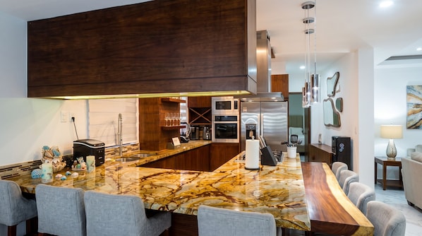 A modern kitchen with a marble countertop, built-in appliances, and a dining area with grey upholstered chairs.