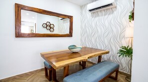 A dining area with a wooden table, a blue bench, a decorative bowl, a mirror, and an air conditioning unit. - The Five Apartments by Monyxbnb (Puerto Vallarta)