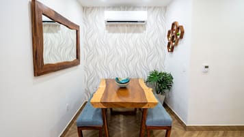 Un comedor con una mesa de madera, dos sillas acolchadas azules, un cuenco decorativo, una planta en maceta y un aire acondicionado de pared.