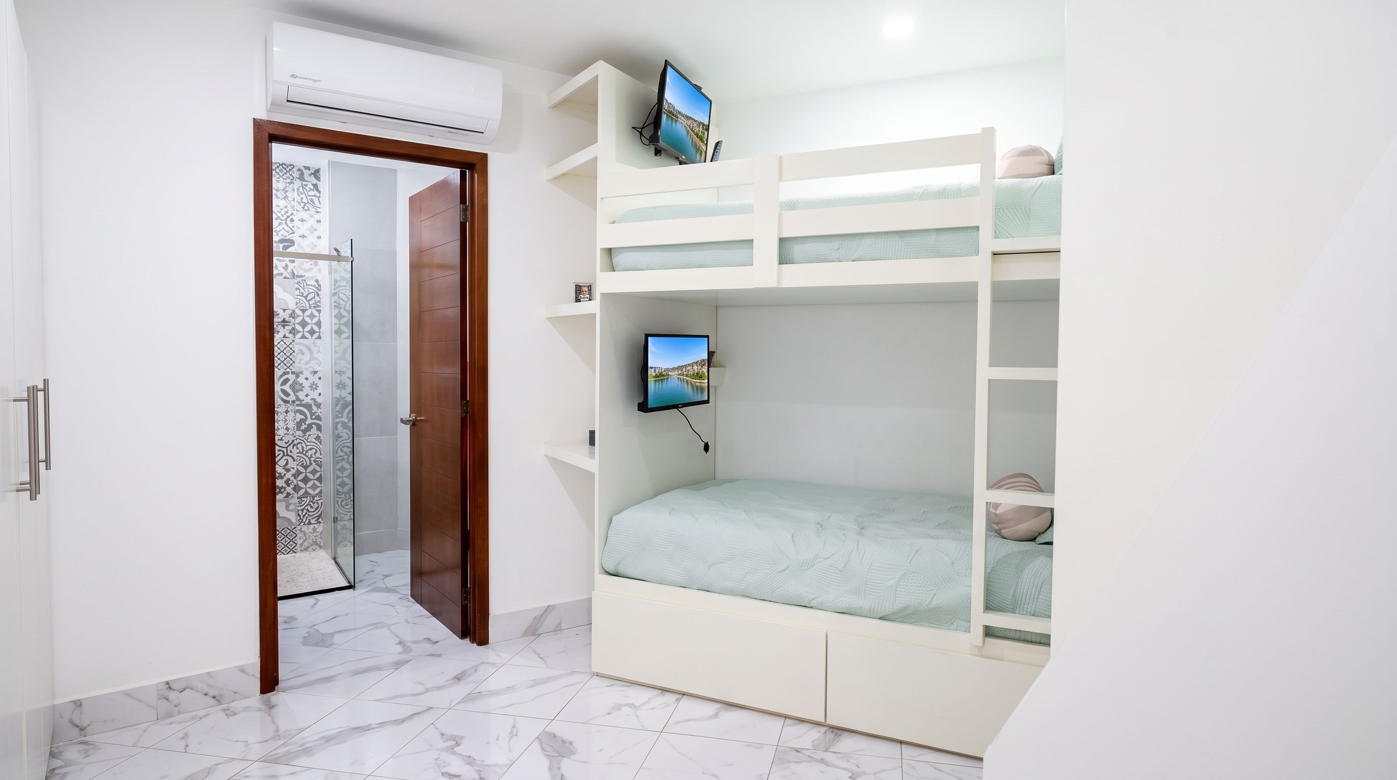A bedroom with a bunk bed, a television mounted on the wall, and a door leading to a bathroom.