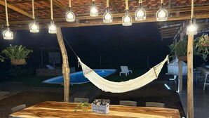 An outdoor dining area with a wooden table and chairs, surrounded by hanging light fixtures. - Luxury Modern Ranch, Private Pool & Farm Animals (santa cruz)