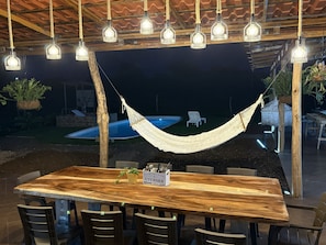 An outdoor dining area with a wooden table and chairs, surrounded by hanging light fixtures. - Luxury Modern Ranch, Private Pool & Farm Animals (santa cruz)