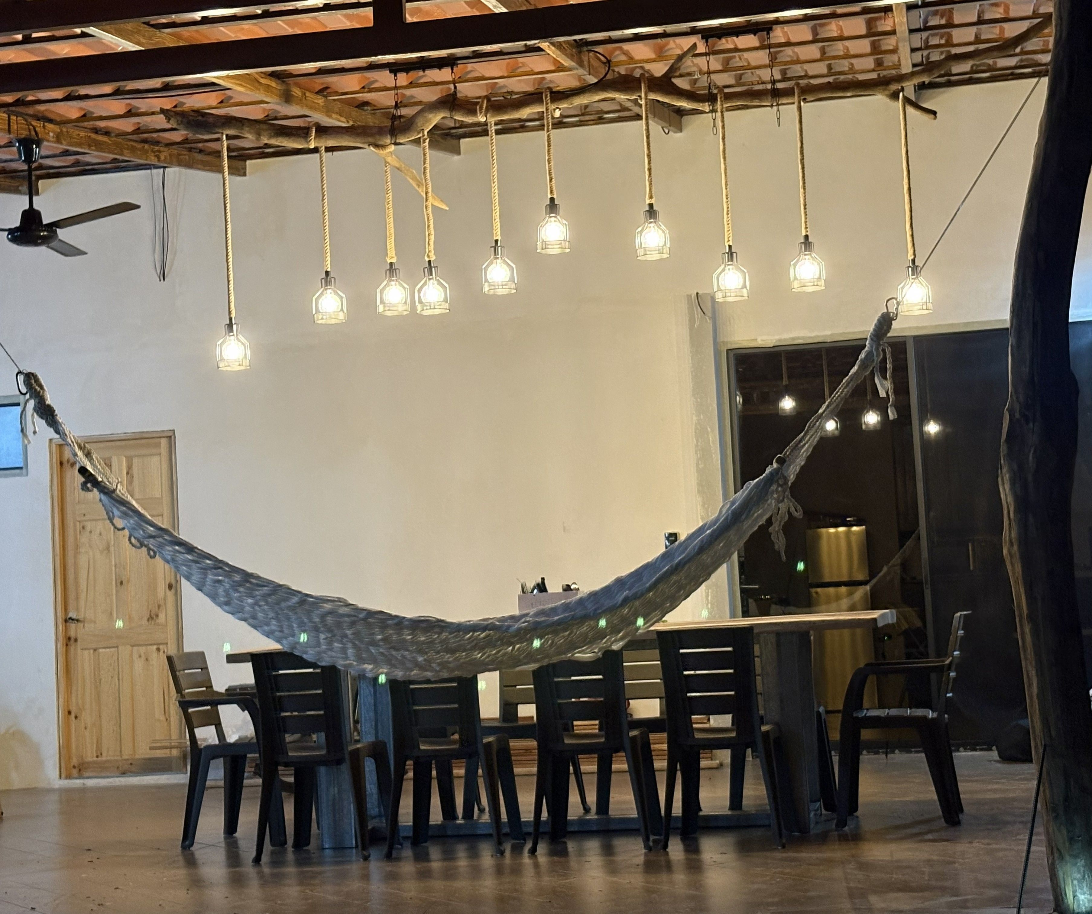 A hammock suspended between chairs in a room with a high ceiling and exposed beams.