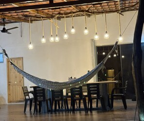A hammock suspended between chairs in a room with a high ceiling and exposed beams.