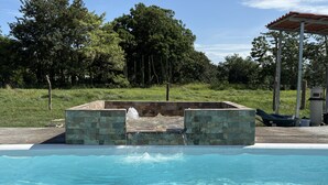 A swimming pool with a stone structure in the center, surrounded by greenery. - Luxury Modern Ranch, Private Pool & Farm Animals (santa cruz)