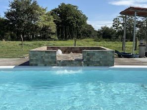 A swimming pool with a stone structure in the center, surrounded by greenery. - Luxury Modern Ranch, Private Pool & Farm Animals (santa cruz)