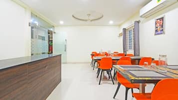 Habitación de hotel con mostrador de recepción, zona de comedor con sillas anaranjadas y un amplio ventanal con cortinas.