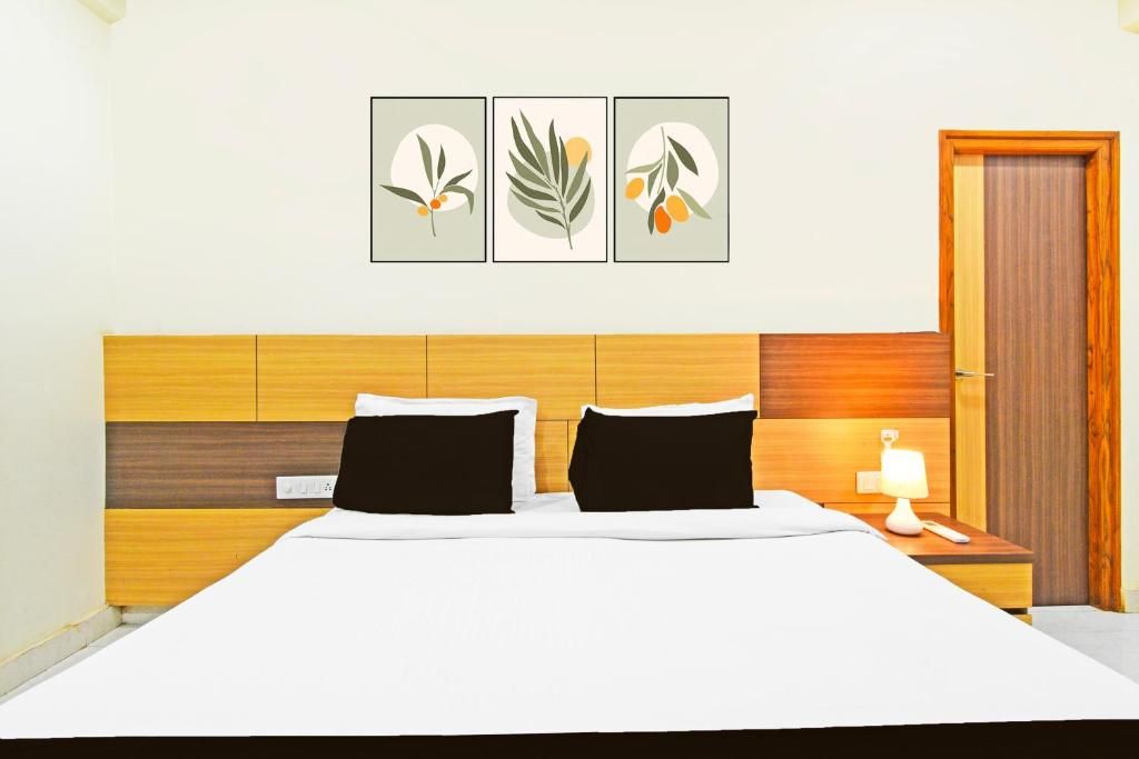 A hotel room with a wooden headboard, a bed with white bedding, a nightstand with a lamp, and three framed botanical prints on the wall.