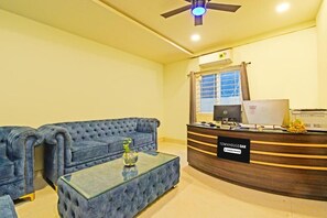 Uma área de recepção com um sofá azul, uma mesa de centro de vidro e um balcão de atendimento.