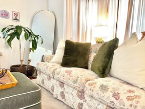 Ein Wohnzimmer mit einem blumigen Sofa, einer Zimmerpflanze und einem Spiegel.