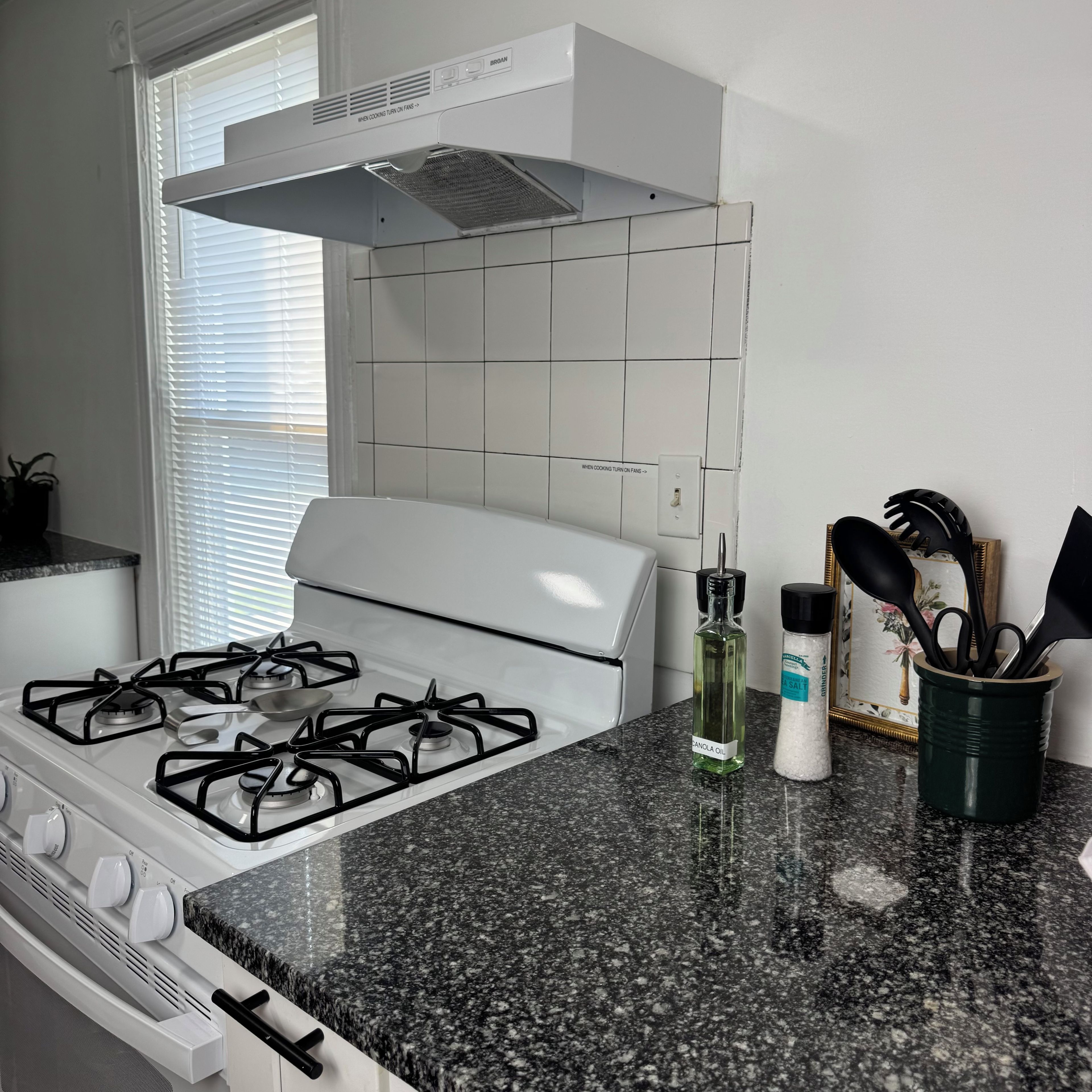 A kitchen with a gas stove, a range hood, and a granite countertop.