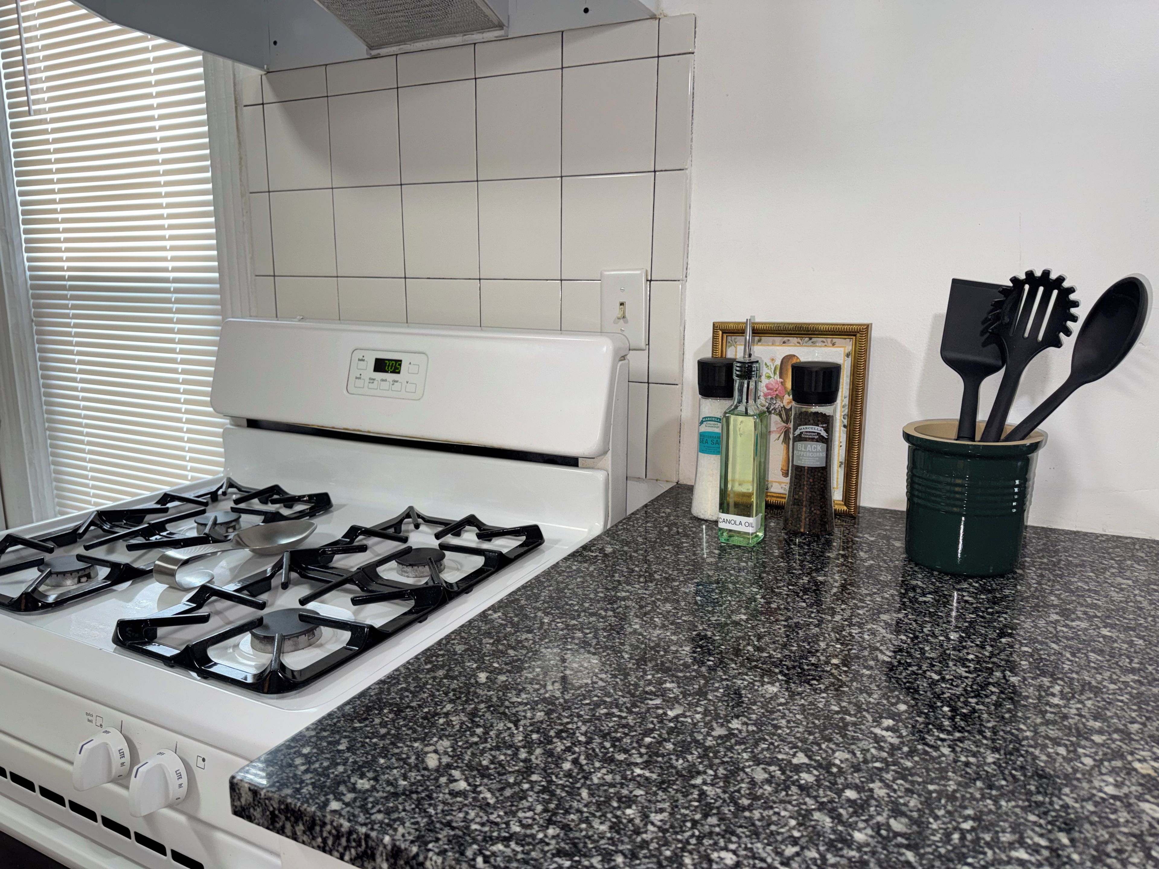 A kitchen with a white stove, granite countertop, and a window with blinds.
