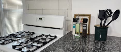 Une cuisine avec un fourneau blanc, un plan de travail en granit et une fenêtre équipée de stores.