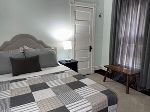 A neatly made bed with a checkered bedspread, a bedside lamp, a wooden nightstand, and a door with a handle.