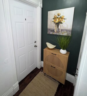 A hallway with a white door, a brown cabinet with handles, a beige rug, and a painting of yellow flowers on the wall.