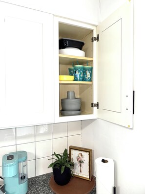 A kitchen with a cabinet containing bowls, cups, and a coffee maker.