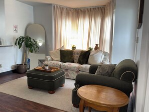 Un salon avec un canapé, un pouf et une table ronde en bois.