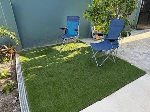 Un pequeño espacio al aire libre con césped artificial, dos sillas plegables azules y una planta en maceta.