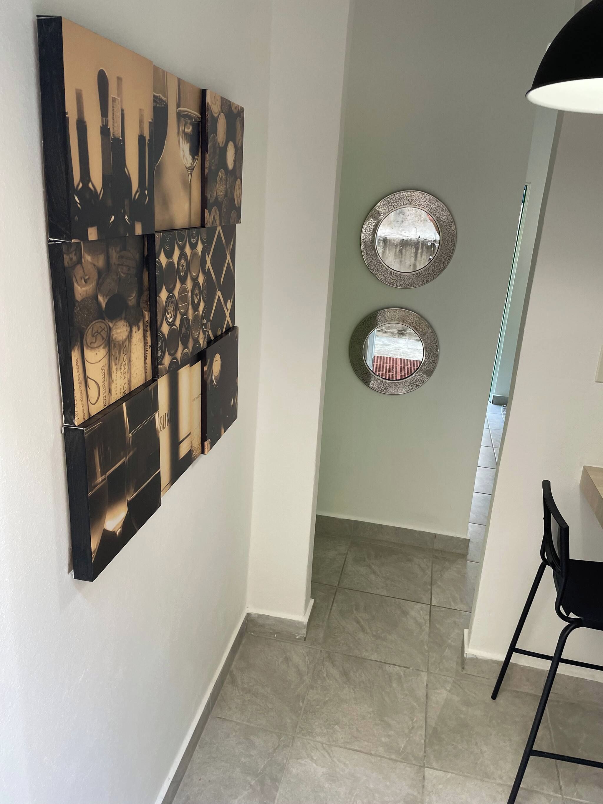 A hallway with a large abstract painting on the wall, two round mirrors, and a chair.