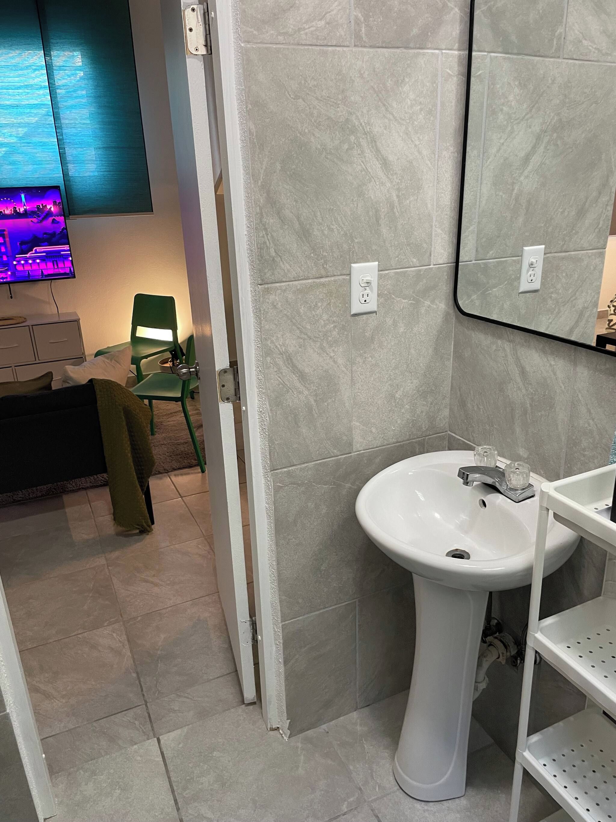 A bathroom with a white sink, a mirror, and a green chair.