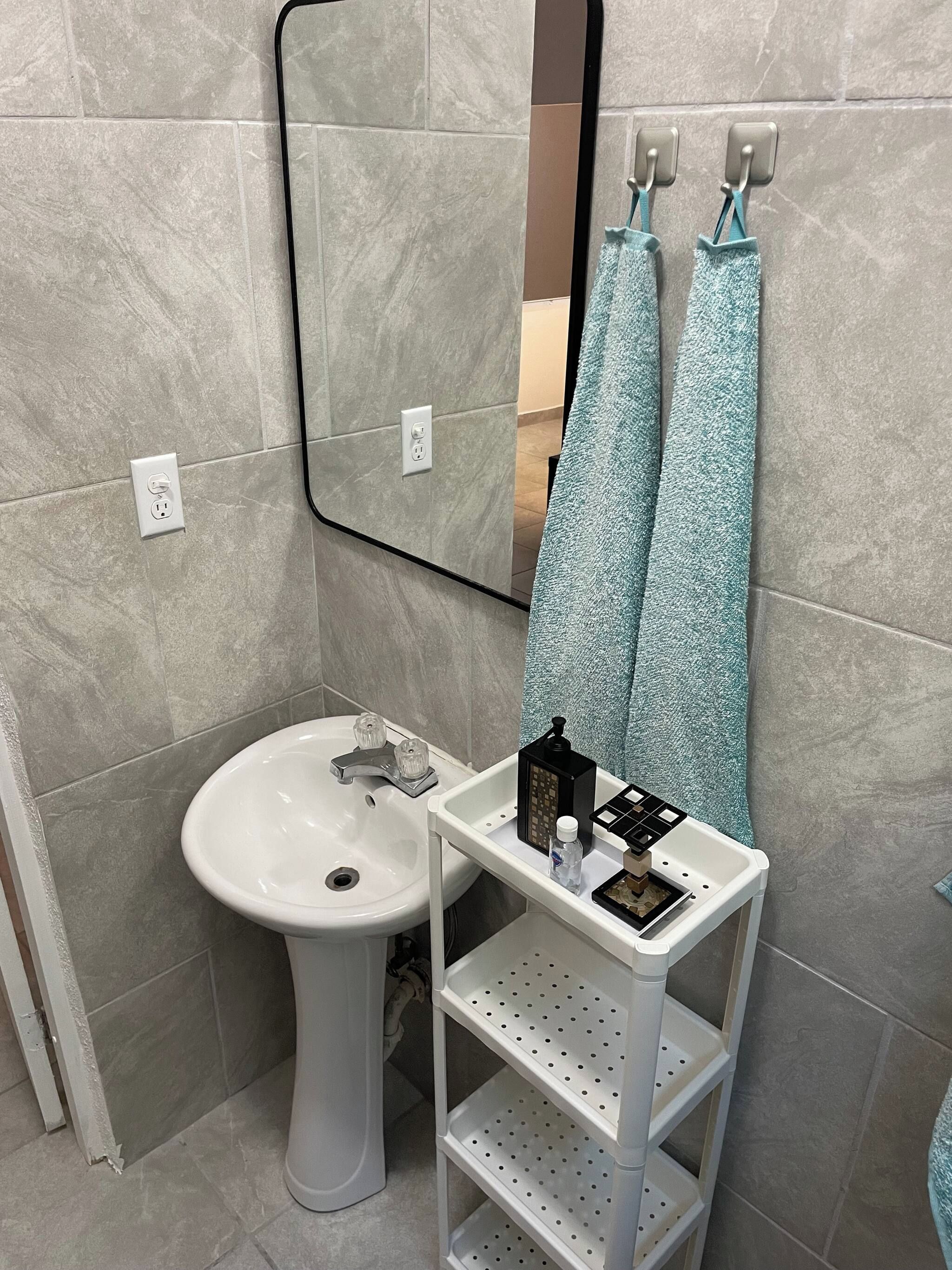 Un bany amb un lavabo pedestal, un mirall, una barra de tovalloles amb dues tovalloles i una petita estant amb productes de tocador.