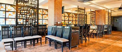 A spacious indoor area with wooden flooring, multiple seating arrangements, and a modern design with geometric patterns on the walls.