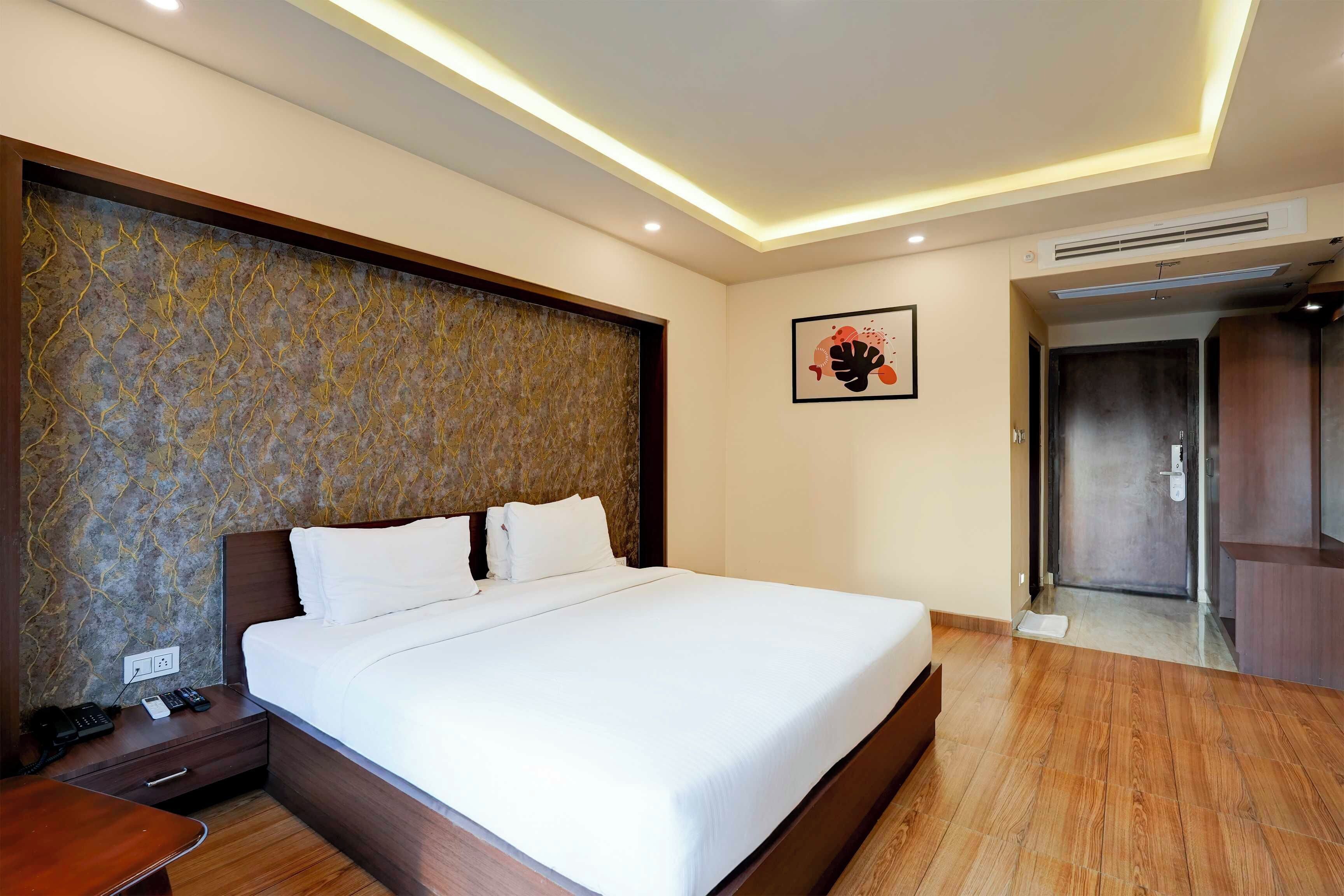 Ein Hotelzimmer mit einem großen Bett, einem Nachttisch aus Holz, einem Telefon und einem an der Wand hängenden Kunstwerk.
