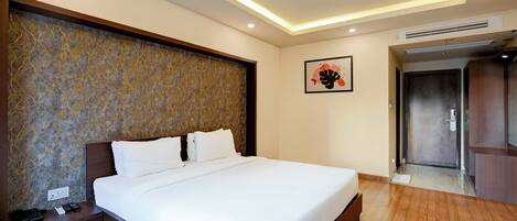 A hotel room with a large bed, a wooden nightstand, a telephone, and a wall-mounted artwork.