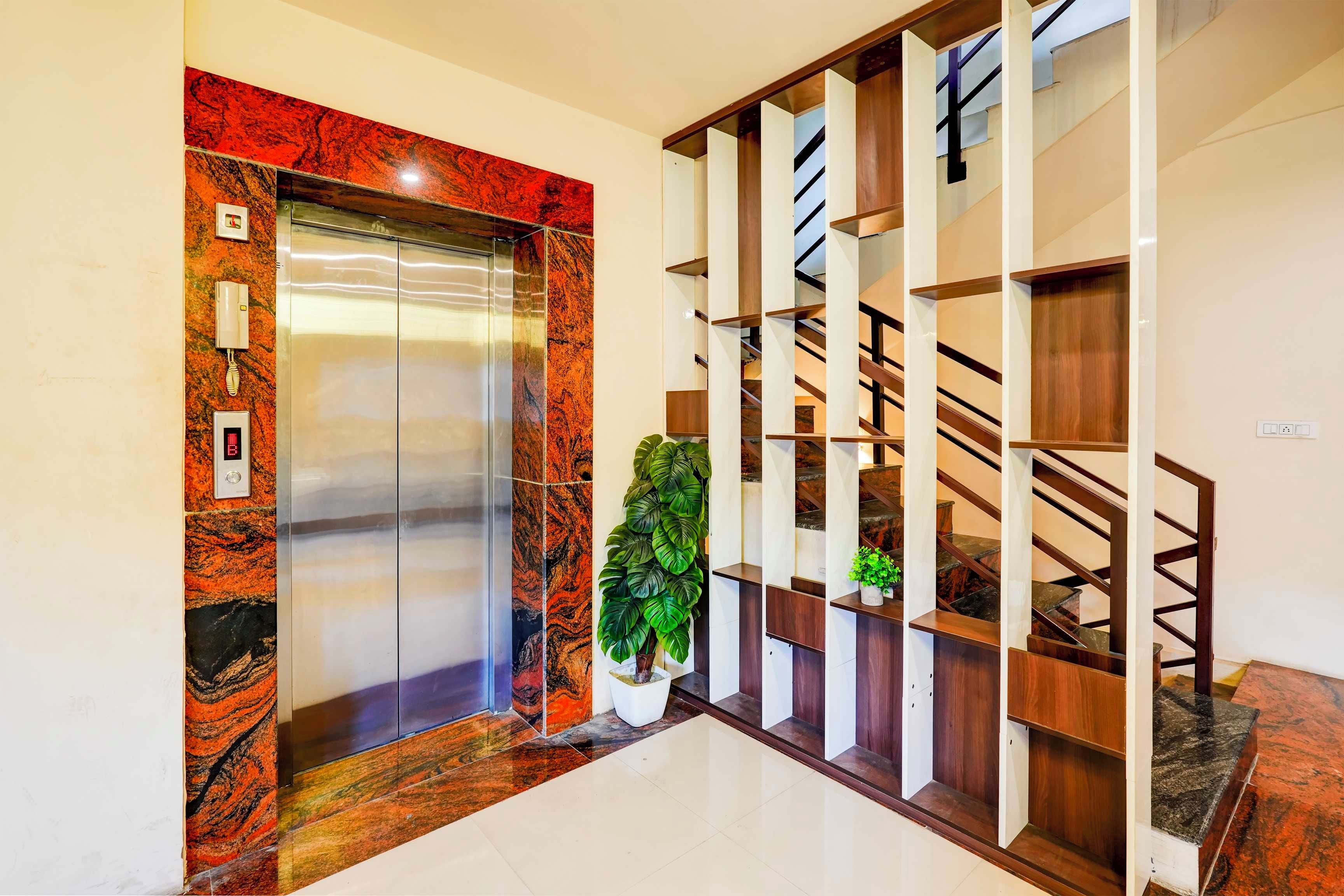Un ascensor con detalles de mármol, una escalera con barandillas de madera y una planta en maceta.