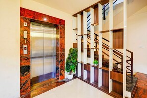 An elevator with a marble finish, a staircase with wooden railings, and a potted plant.