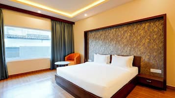 A hotel room with a large bed, a small round table, a chair, and a view of a bridge through the window.
