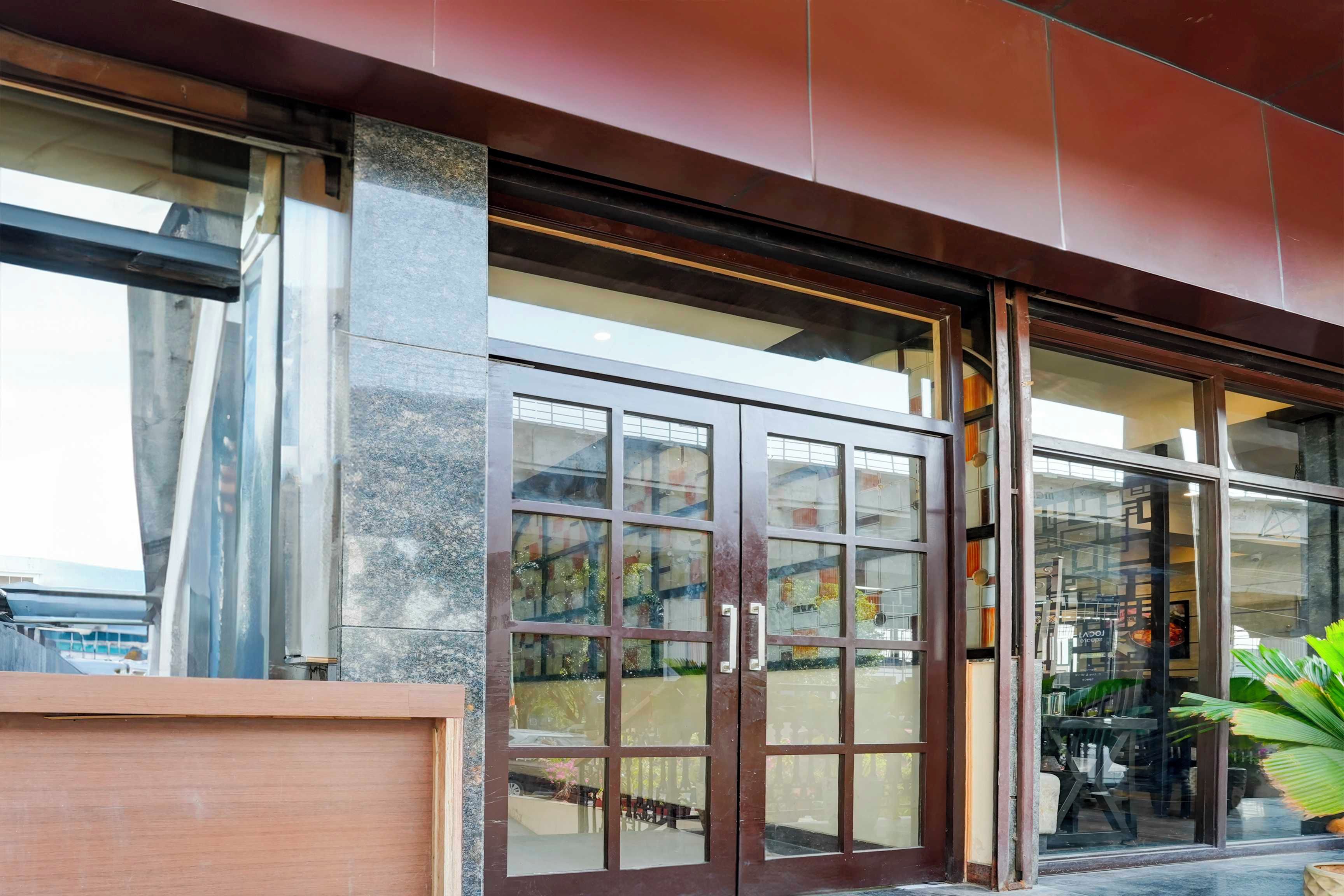 Una entrada de edificio moderna con grandes puertas y ventanas de vidrio, un pilar de concreto y un toldo de metal.