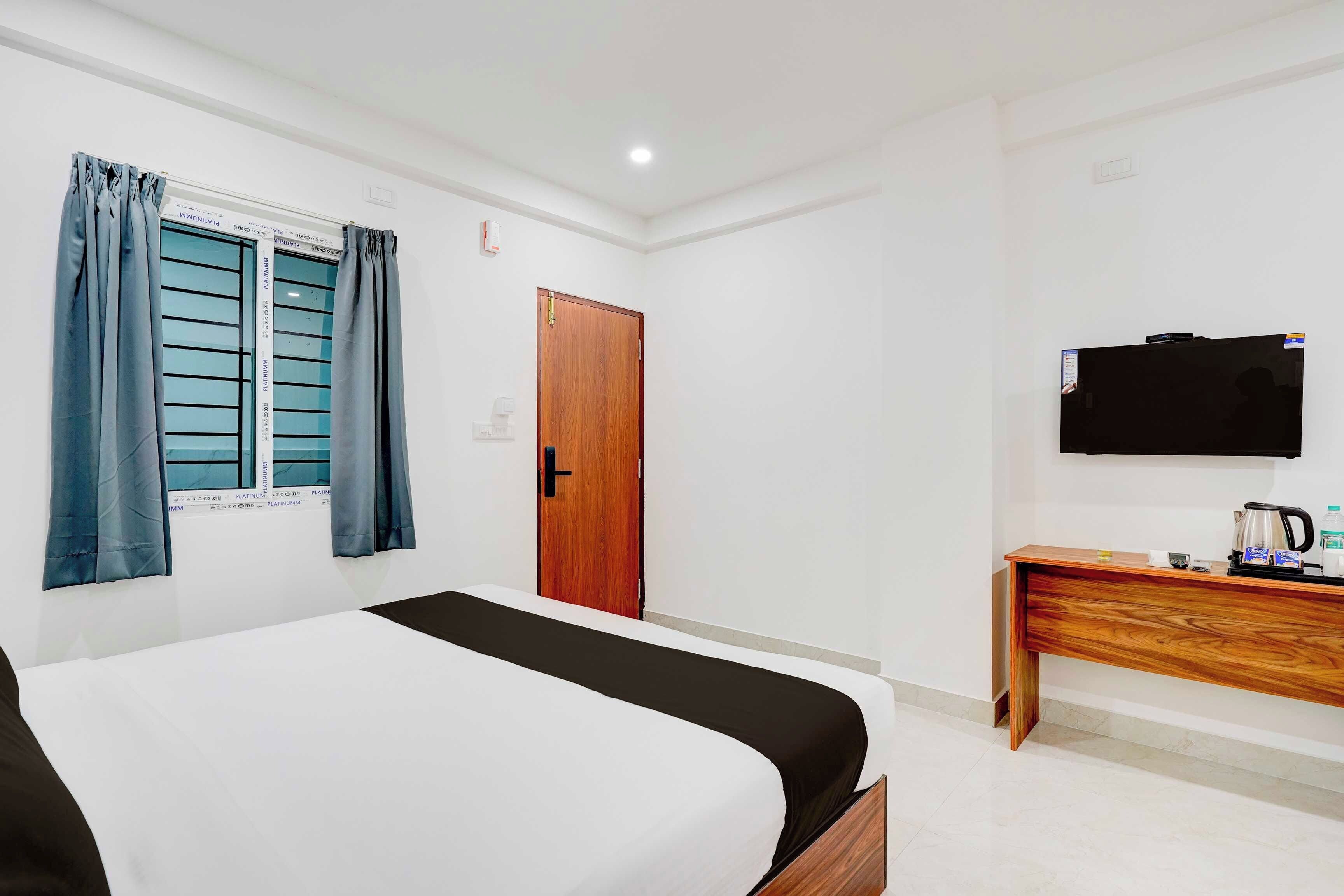 A hotel room with a bed, a wooden desk, a television, and a window with curtains.