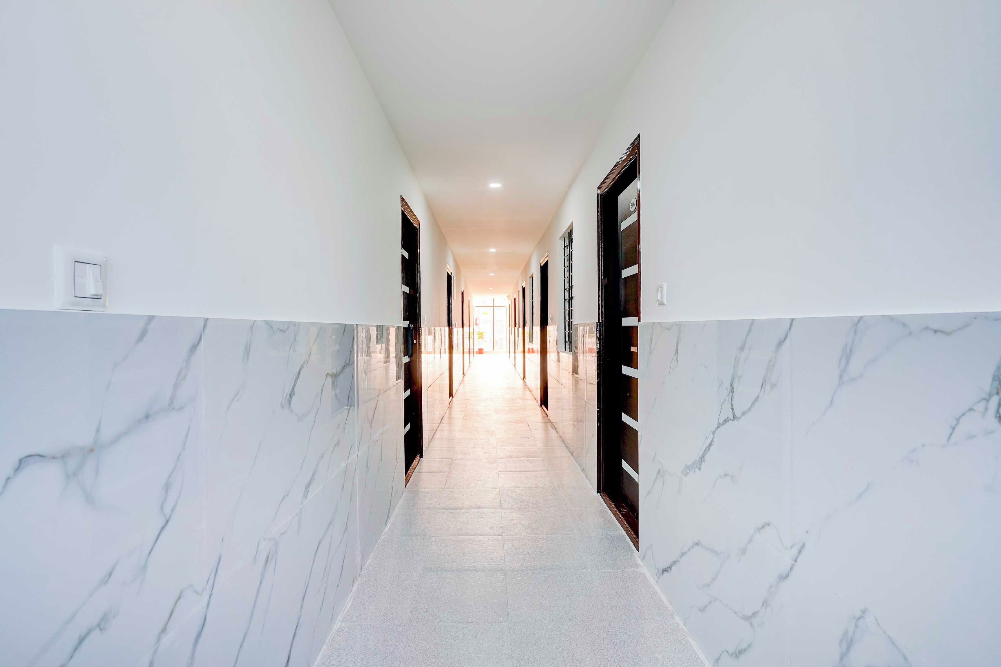 A corridor with marble walls and doors, leading to a bright room at the end.