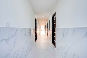 A corridor with marble walls and doors, leading to a bright room at the end.