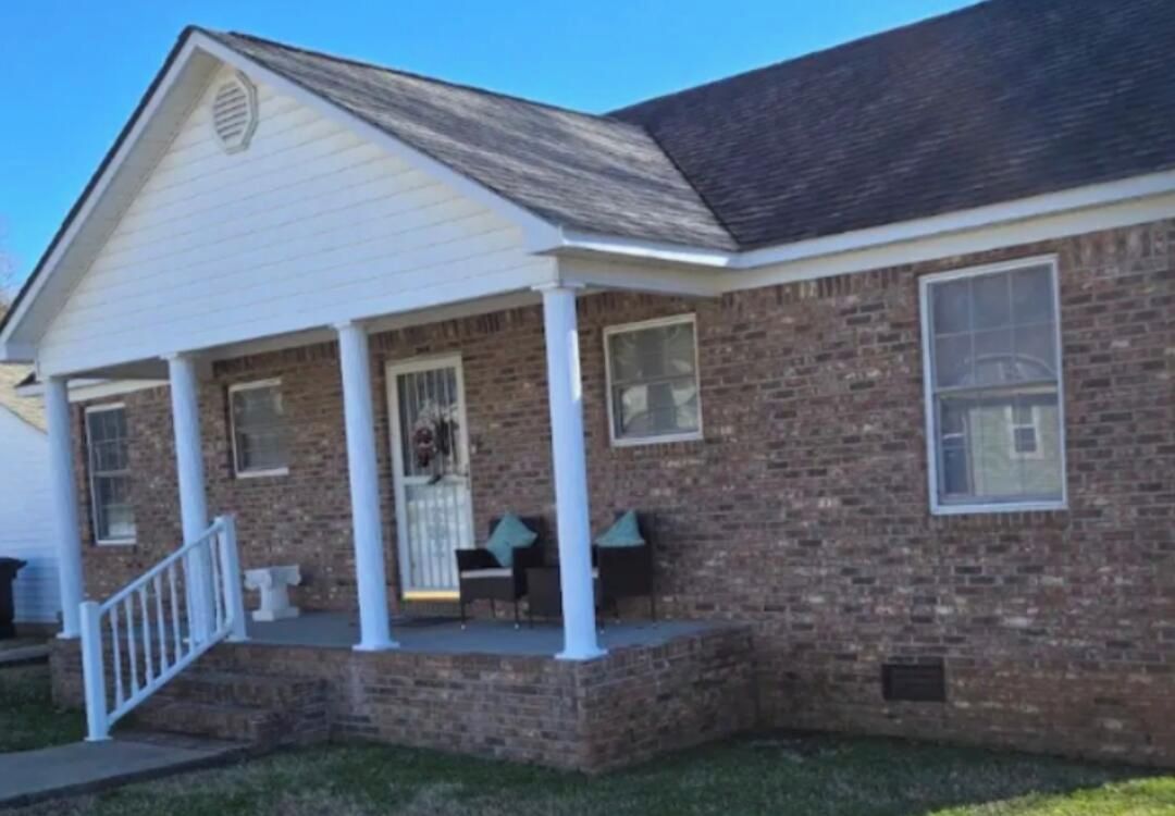 A two-story brick house with a front porch, a white door, and a window on the second floor.