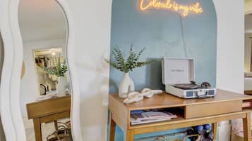 A room with a large mirror, a neon sign, a wooden console table, woven baskets, and a vinyl record player.