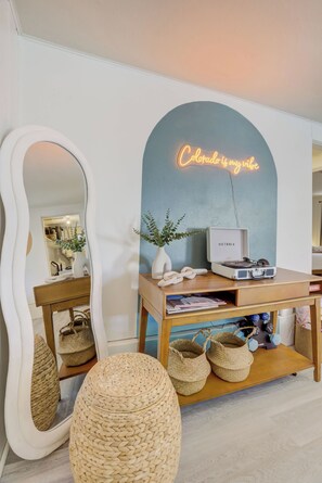 Quarto com espelho grande, luminária de neon, mesa consola de madeira, cestos de fibra e toca-discos de vinil.