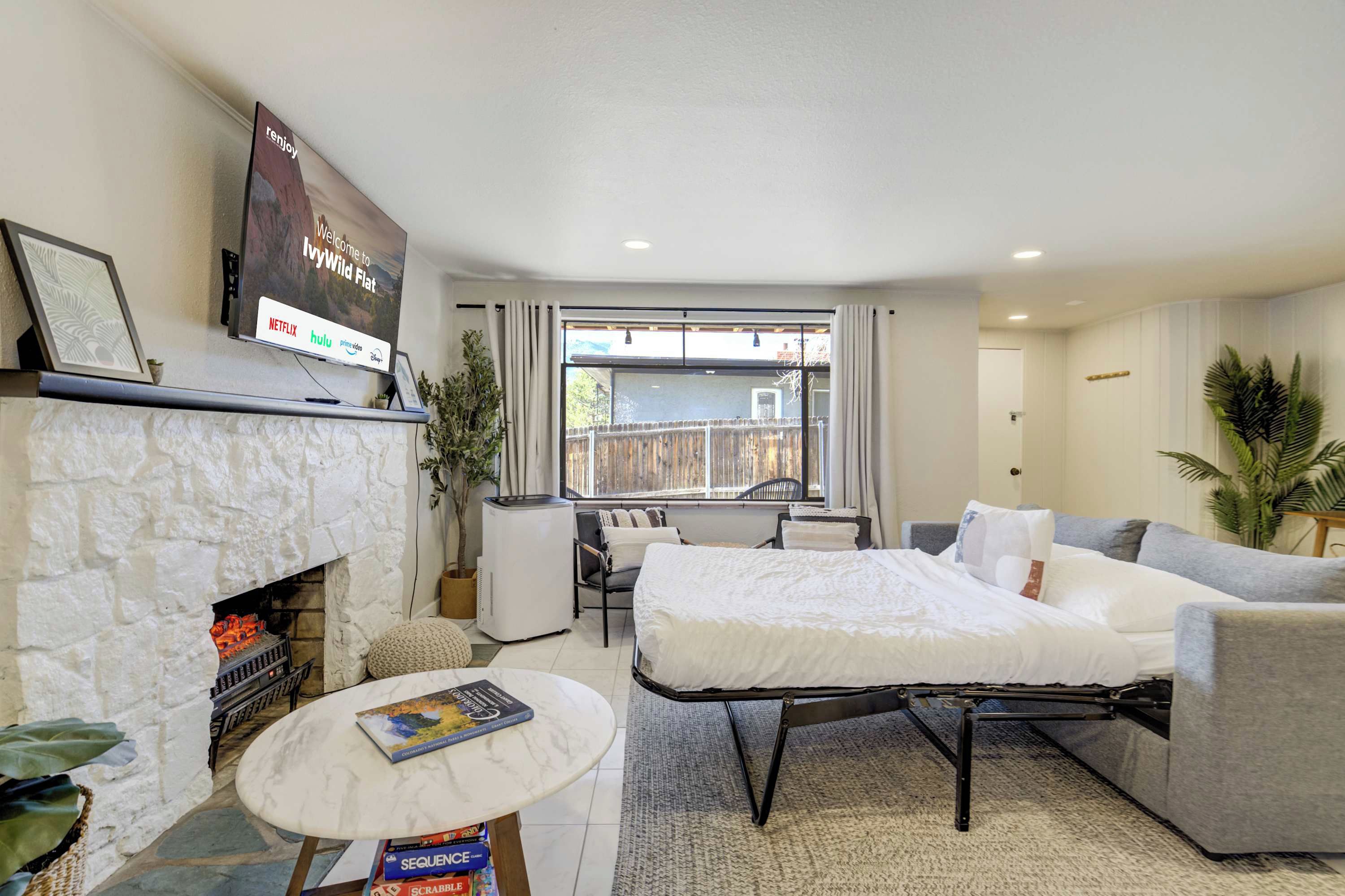 A modern living room with a fireplace, a flat-screen TV, a sofa, a coffee table, and a view of the outside.