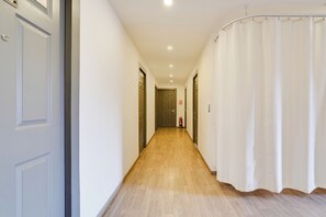 A hallway with wooden flooring, white walls, and a white curtain on the right.