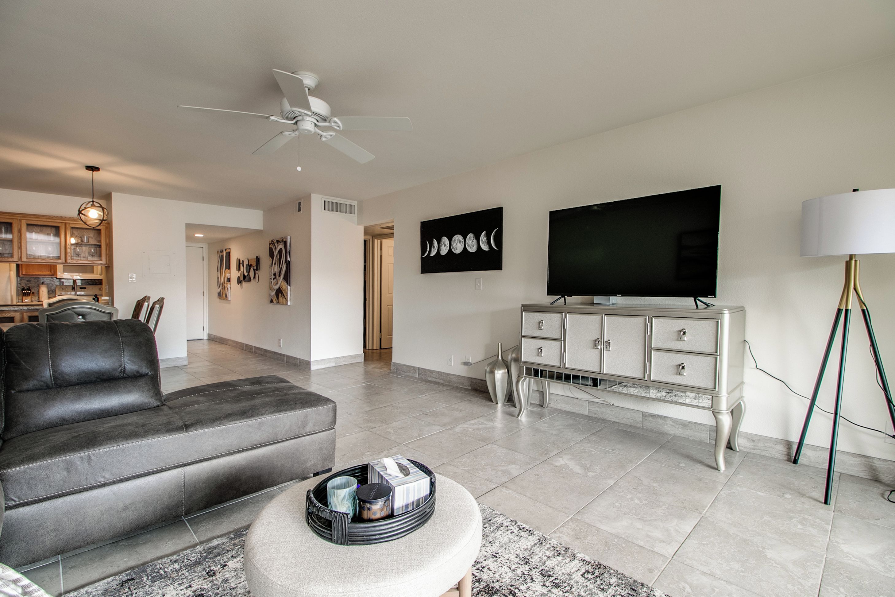 A modern living room with a grey sofa, a flat-screen TV, a white cabinet, and a ceiling fan.