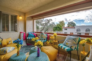 A balcony with yellow and blue furniture, a view of trees and buildings, and a decorative vase with flowers. - Old Town Pool + Hot Tub Free Parking (Scottsdale)