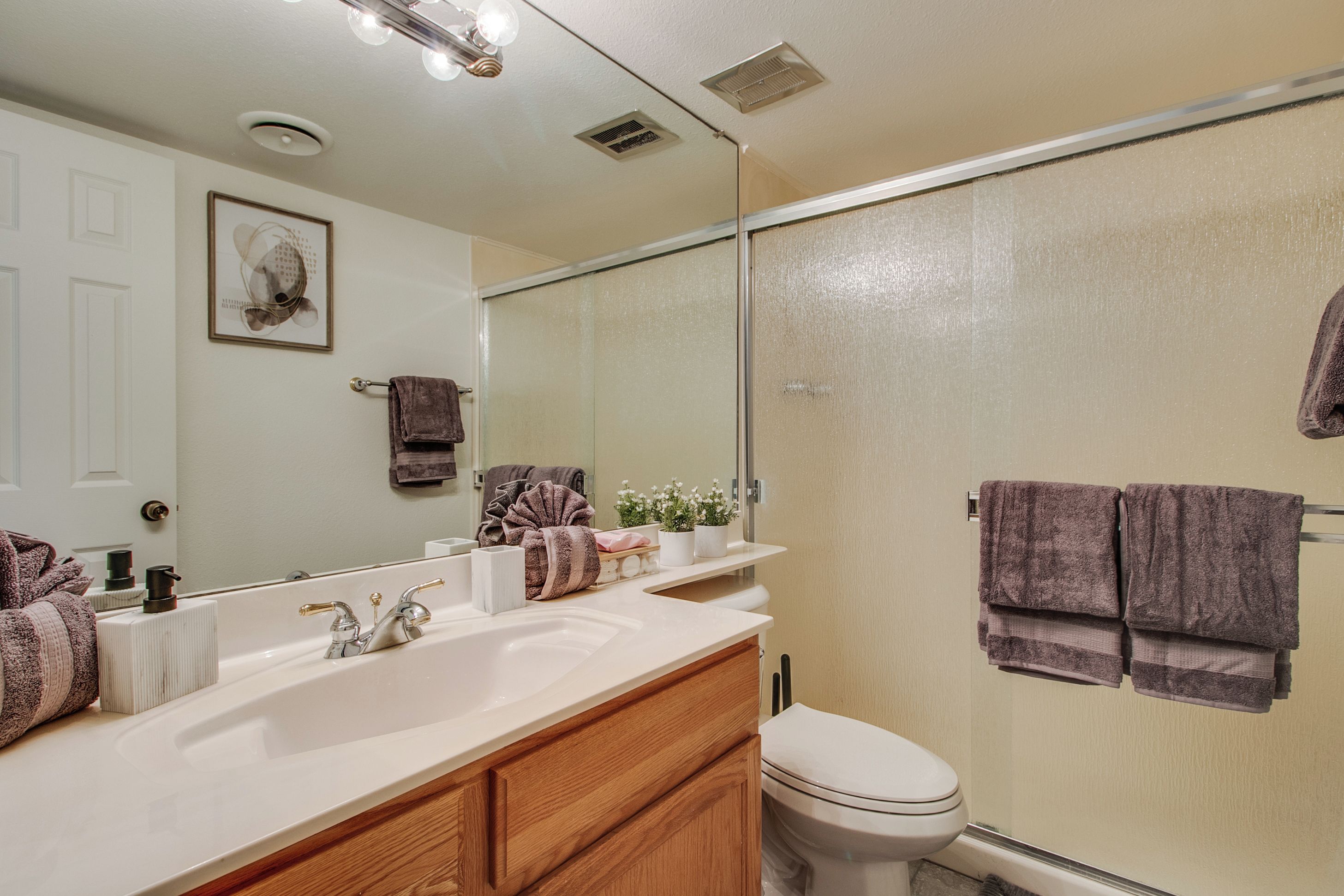 Une salle de bain avec un lavabo blanc, un meuble-lavabo en bois, un miroir, des toilettes et un espace douche.