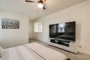 Ein Schlafzimmer mit einem Bett, einem Deckenventilator, einem Fernseher auf einem Marmorkorpus und einem Fenster mit Jalousien.