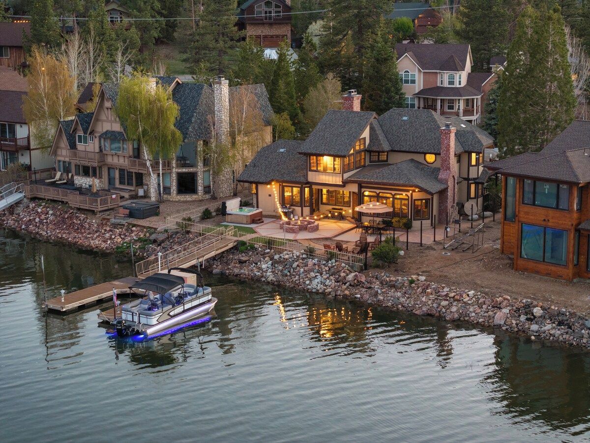 A lakeside property with a dock, a boat, and multiple houses with outdoor seating areas.