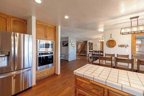 A modern kitchen with stainless steel appliances, wooden cabinets, and a dining area with a tiled table. - Big Bear Lakefront | Dock, Hot Tub & Game Room (Big Bear Lake)