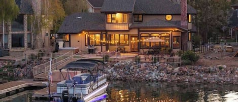 A lakeside house with a dock, a boat, and a stone chimney.