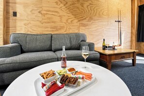 A modern living room with a grey sofa, a round coffee table with snacks and a bottle, and a wine glass. - The Black Barn - Whakatane Holiday Home (Whakatane)