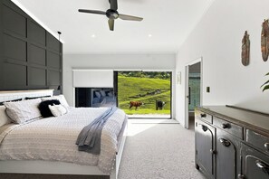Un dormitorio moderno con una cama, ventilador de techo, cómoda y vista a un paisaje verde a través de una puerta abierta.